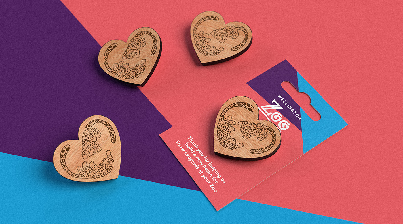 The snow leopard pins for Wellington Zoo, displayed on a coral pink and blue background, designed by Bradley Pratt